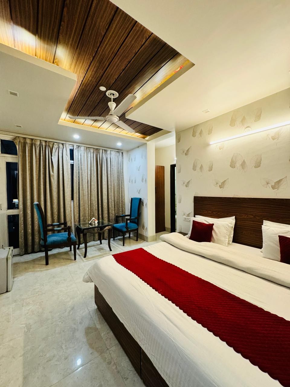 A modern hotel room with a large bed, two chairs, a small table, and a ceiling fan.