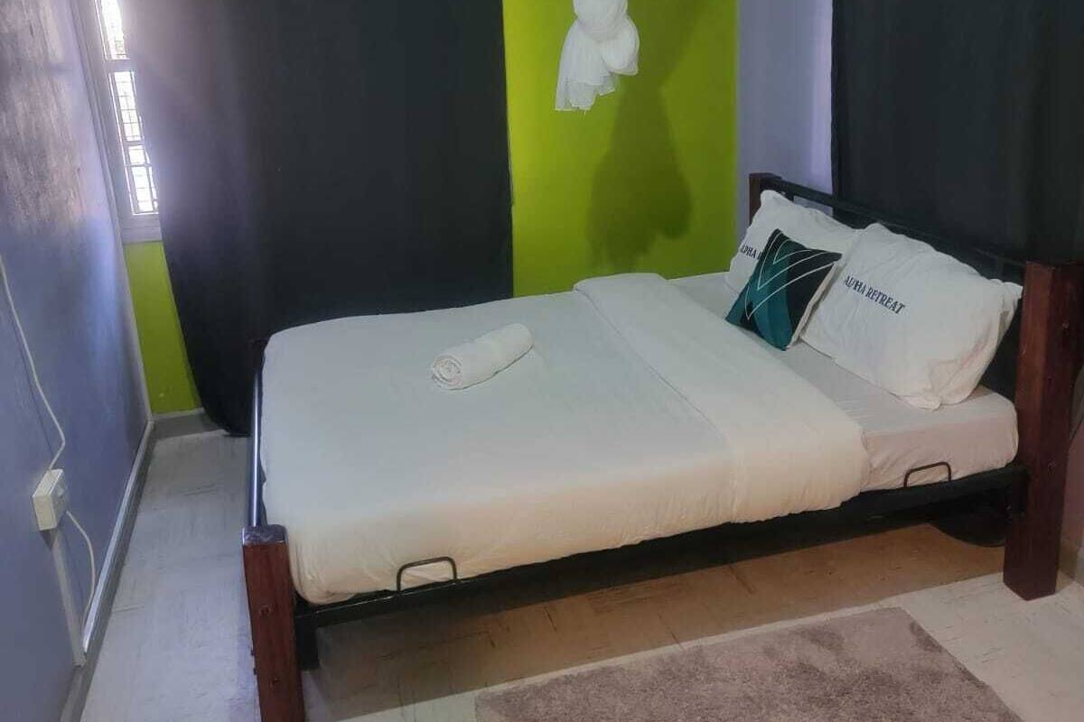 Ein Einzelbett mit weißer Matratze und hölzernem Gestell, ein brauner Teppich und ein Paar grüne Flip-Flops auf dem Boden.