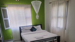A bedroom with a bed, a mosquito net, a window, and a door. - ALPHA RETREAT (Kisumu)