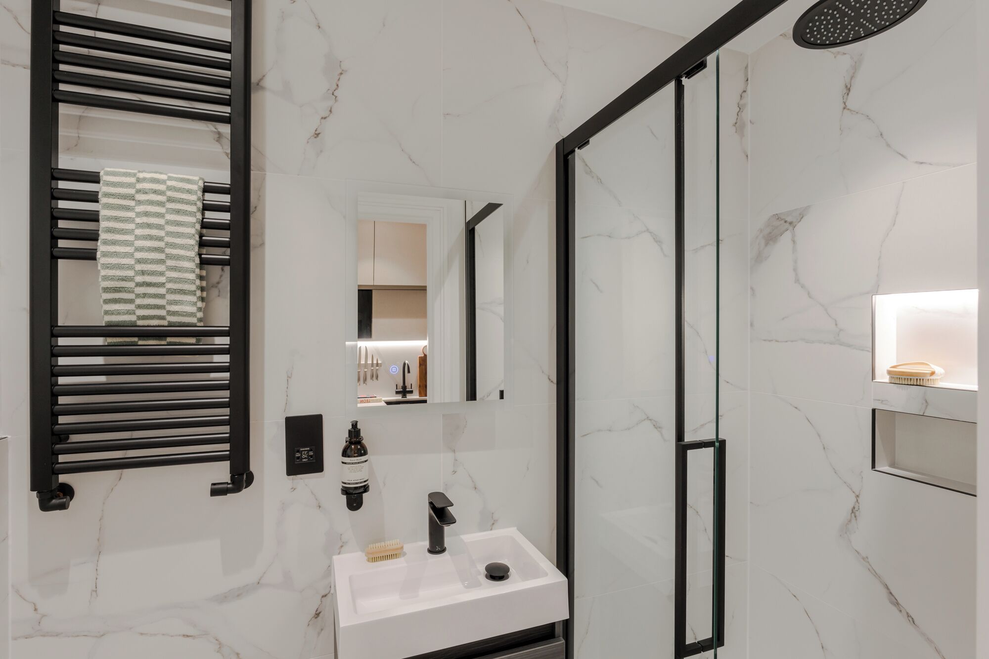 A modern bathroom with a glass shower enclosure, a white sink with a black faucet, and a towel rack with a checkered towel.