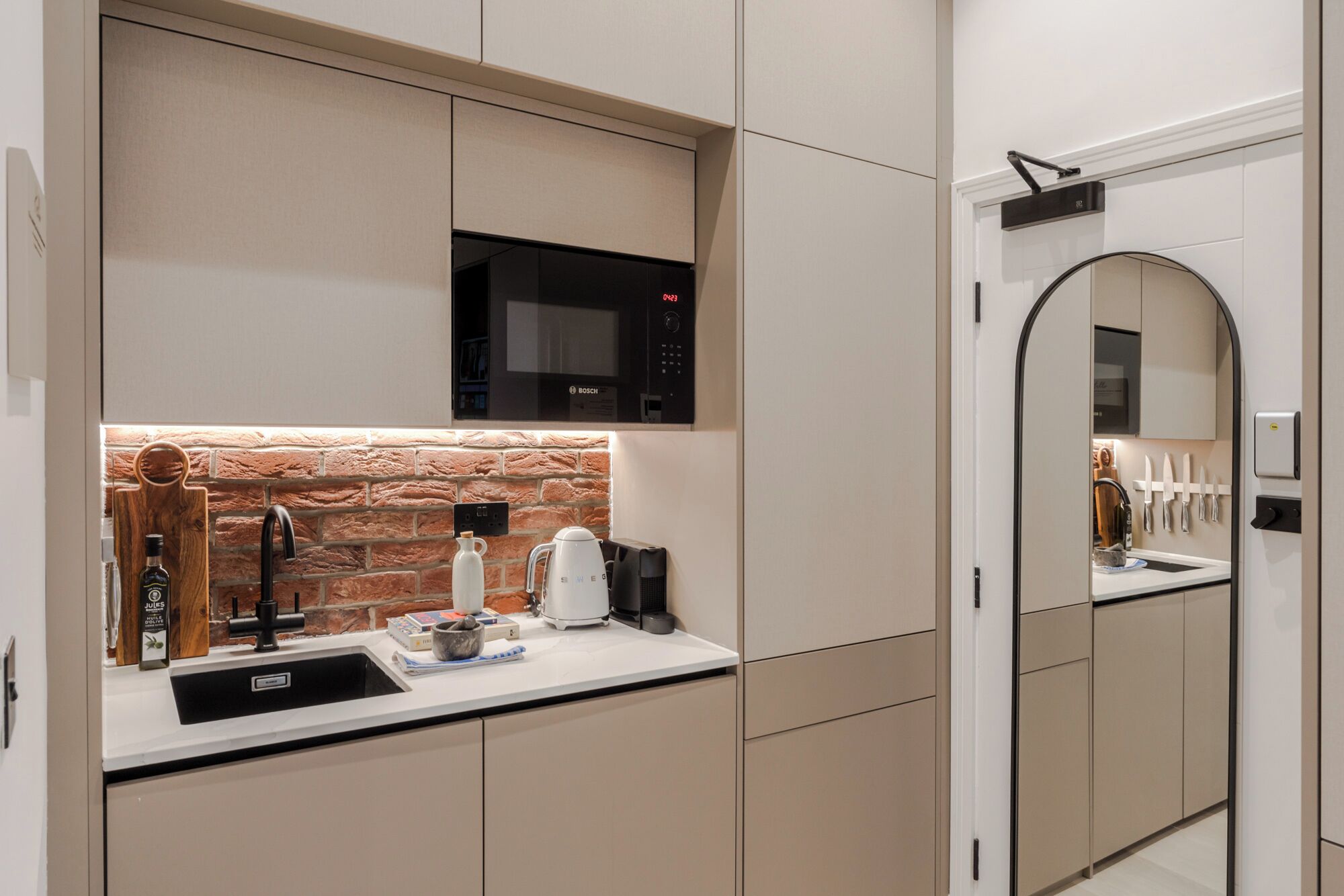 A modern kitchen with a Bosch microwave, a stone backsplash, and a sink with a wooden cutting board and a bottle of Jules.