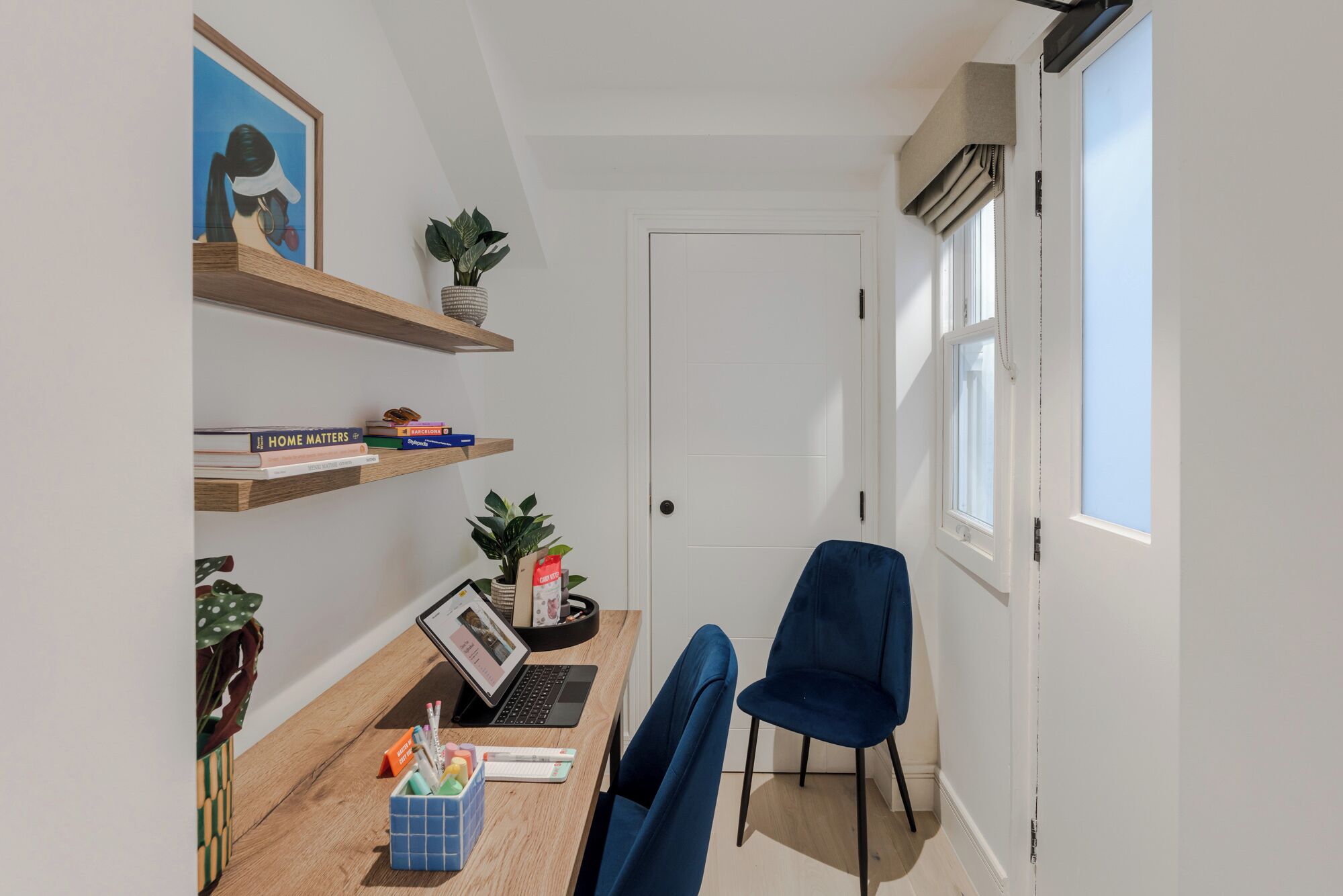 A small, well-lit room with a desk, chair, and shelves containing books and decorative items.