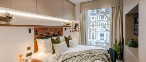 A modern hotel room with a large bed, a desk, and a window with a city view.