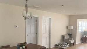A spacious dining area with a wooden table and chairs, a chandelier, and a door leading to another room.