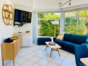 En moderne stue med et stort vindue, et fladskærms-tv, en blå sofa og et træsidebord.