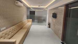 A modern hallway with a beige sofa, a ceiling fan, and a glass door leading to another room. - Hotel Morya Residency Parel (Mumbai)