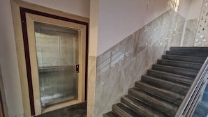 A marble staircase with a metal railing, leading to an elevator with a red button panel. - Hotel Morya Residency Parel (Mumbai)