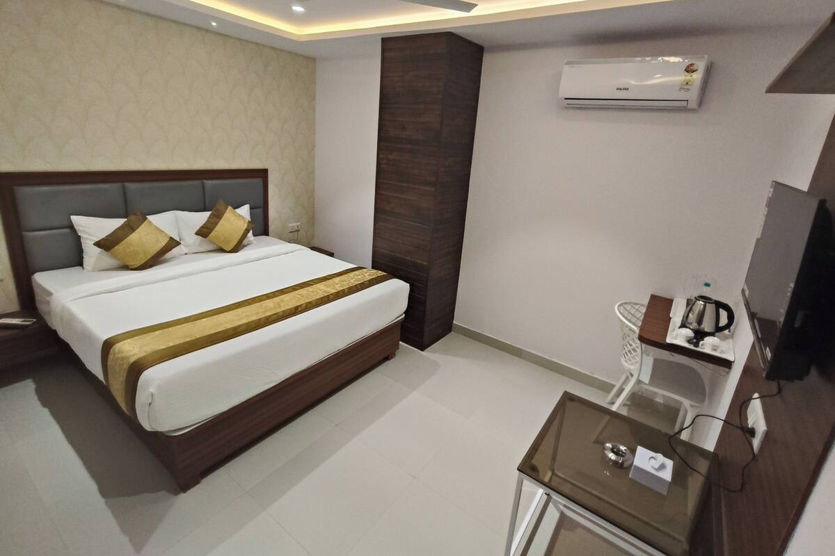 A modern hotel room with a large bed, a bedside table with a kettle, an air conditioning unit, and a ceiling fan.
