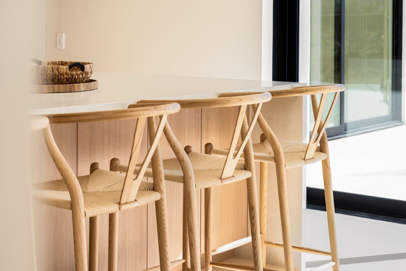 A modern kitchen with wooden bar stools and a woven basket on the counter.