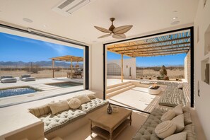 A modern interior with a large window, a pool, and a seating area with a view of the desert. - Villa Luna - Ibiza villa w pool & rooftop deck (Joshua Tree)