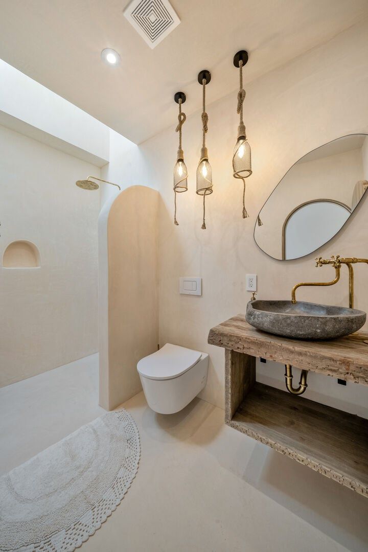 Une salle de bain avec des toilettes blanches, un lavabo en pierre avec un robinet en laiton et un meuble-lavabo en bois.