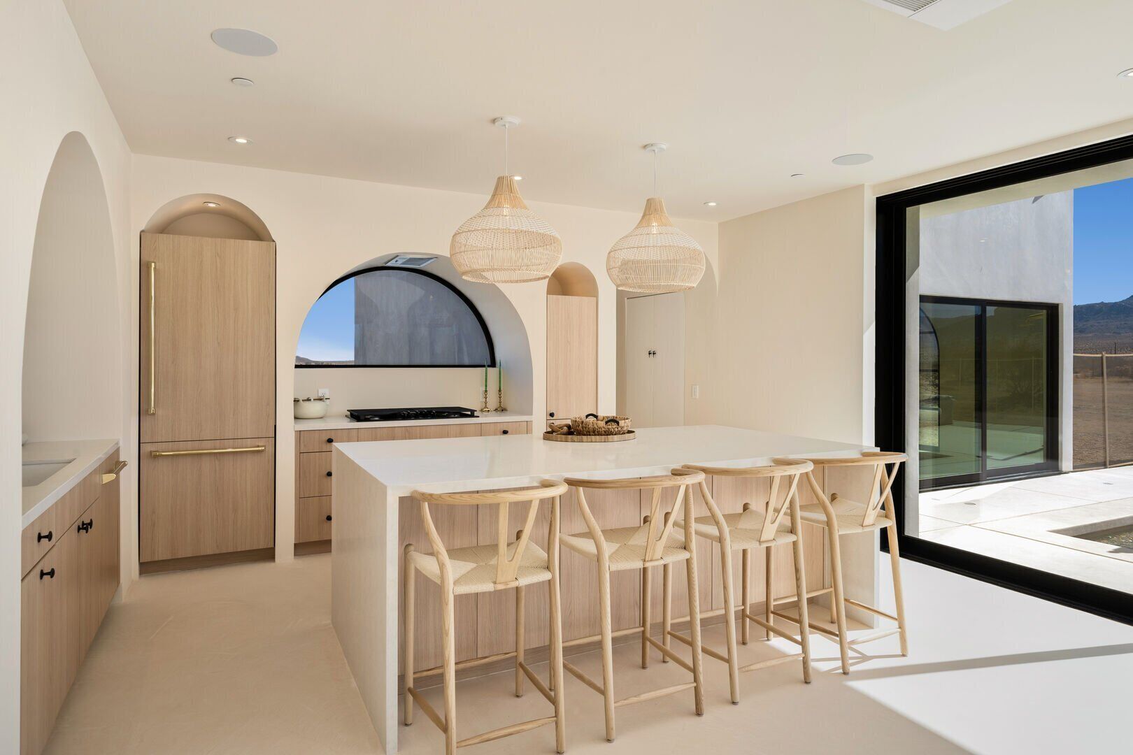 Une cuisine moderne avec un îlot central, des chaises en bois et des luminaires suspendus.