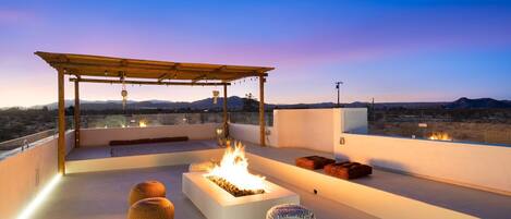 A rooftop terrace with a fire feature, seating, and a pergola.