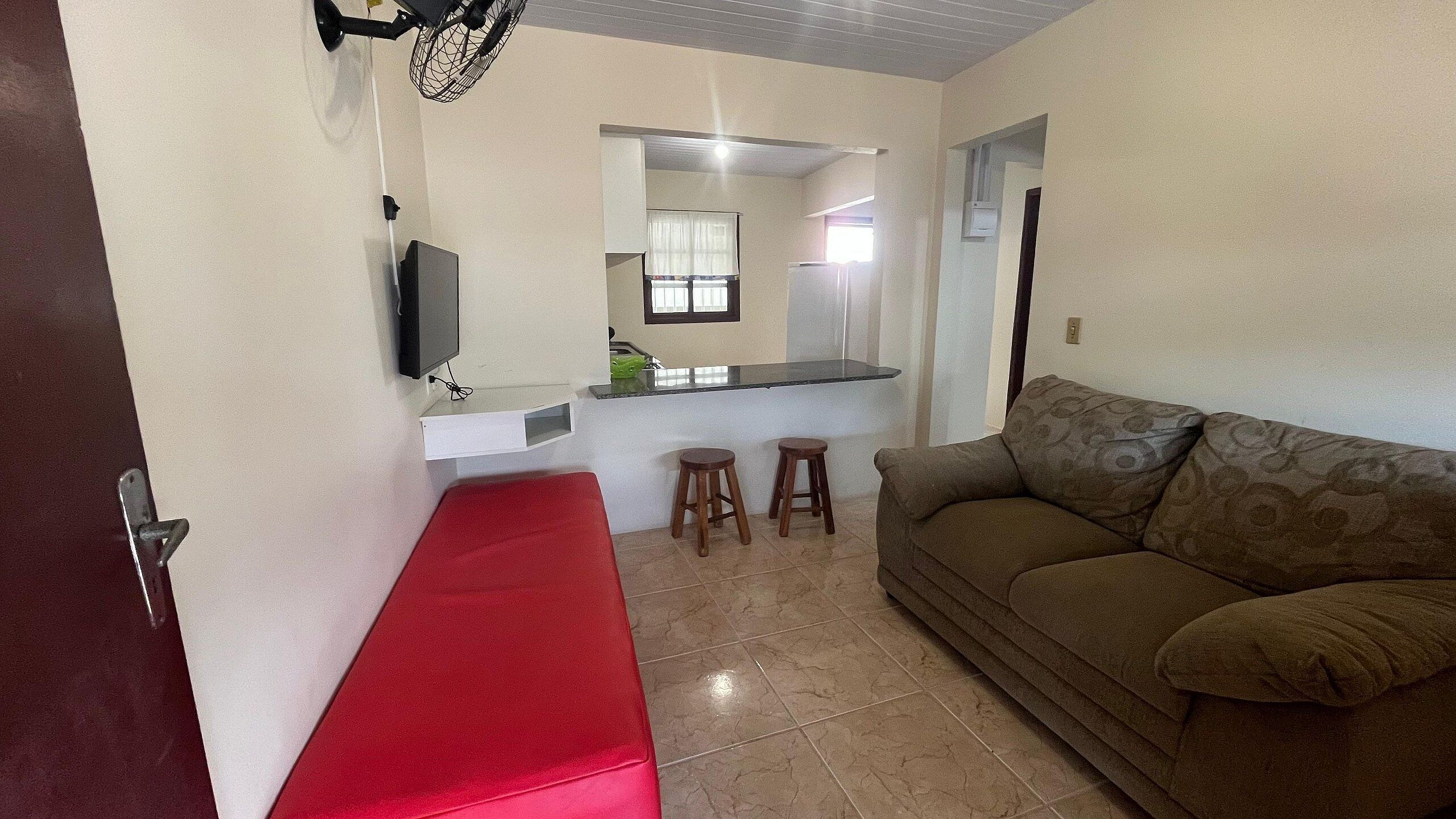A compact living space with a kitchenette, a red bench, two stools, and a patterned sofa.