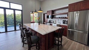A modern kitchen with a central island, stainless steel appliances, and a large window providing a view of the outdoors. - Villa 15 at Chial Reserve Near San Ignacio (San Ignacio)