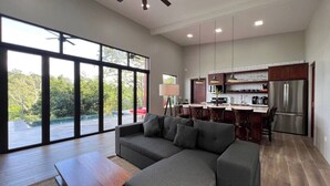 A spacious living area with a large sectional sofa, a wooden coffee table, and a dining area with a kitchen in the background. - Villa 15 at Chial Reserve Near San Ignacio (San Ignacio)