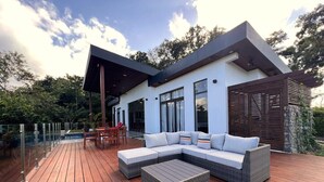 A modern outdoor living area with a wooden deck, a sectional sofa, and a small table. - Villa 15 at Chial Reserve Near San Ignacio (San Ignacio)