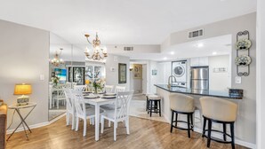 Una cocina moderna con una isla central, taburetes blancos en la barra y un comedor con candelabro.