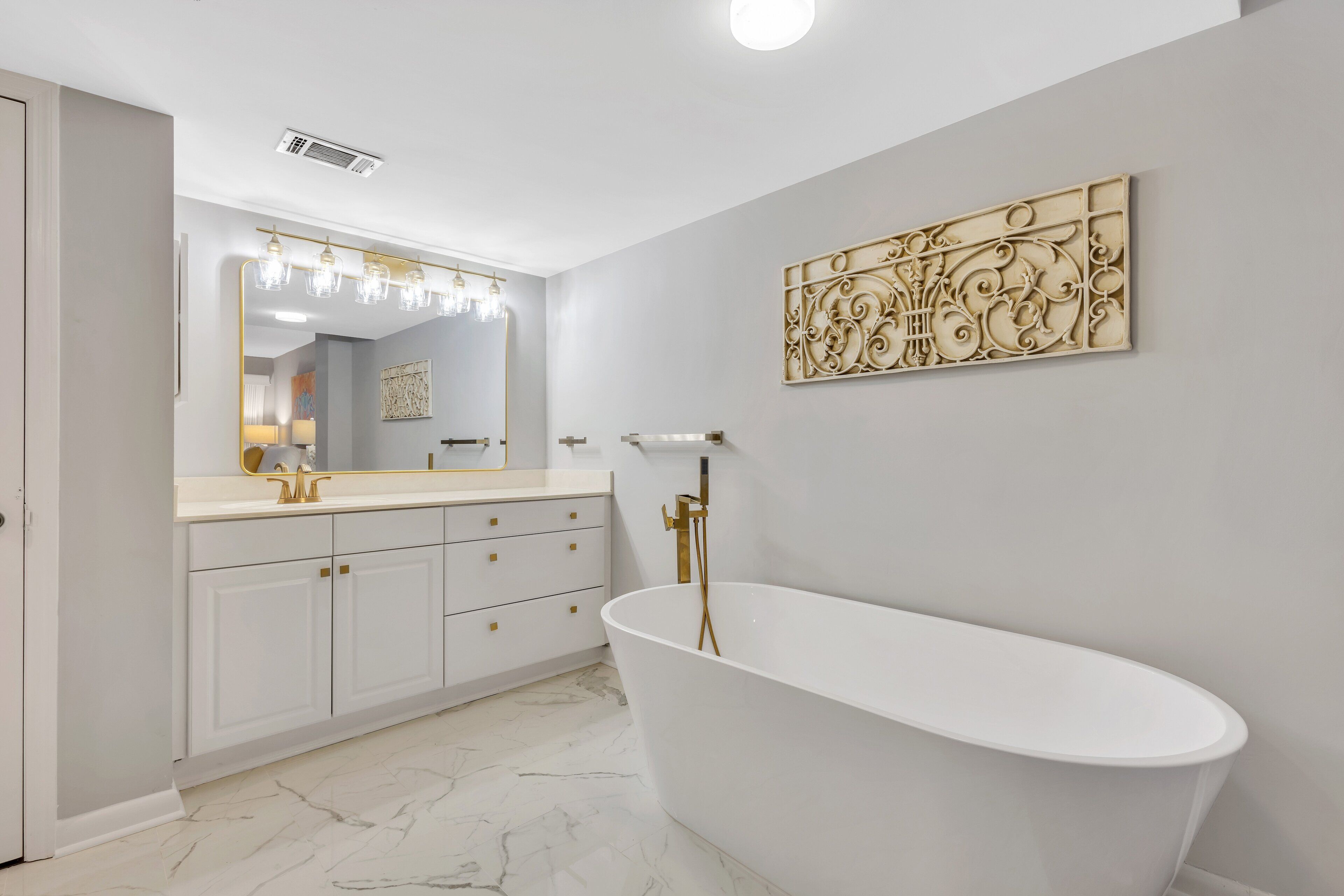 Un baño moderno con una bañera independiente, un tocador con un espejo grande y suelo de mármol.