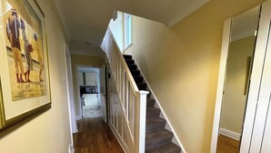 A hallway with wooden flooring, a staircase with a white railing, and a framed picture on the wall. - 1 Lathom Avenue (Morecambe)
