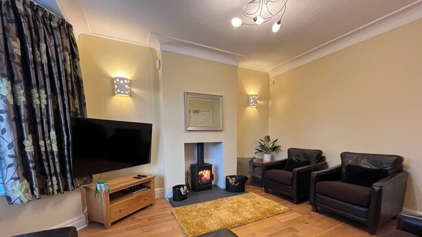 A living room with a flat-screen TV, leather sofas, a fireplace, and a wooden floor. - 1 Lathom Avenue (Morecambe)