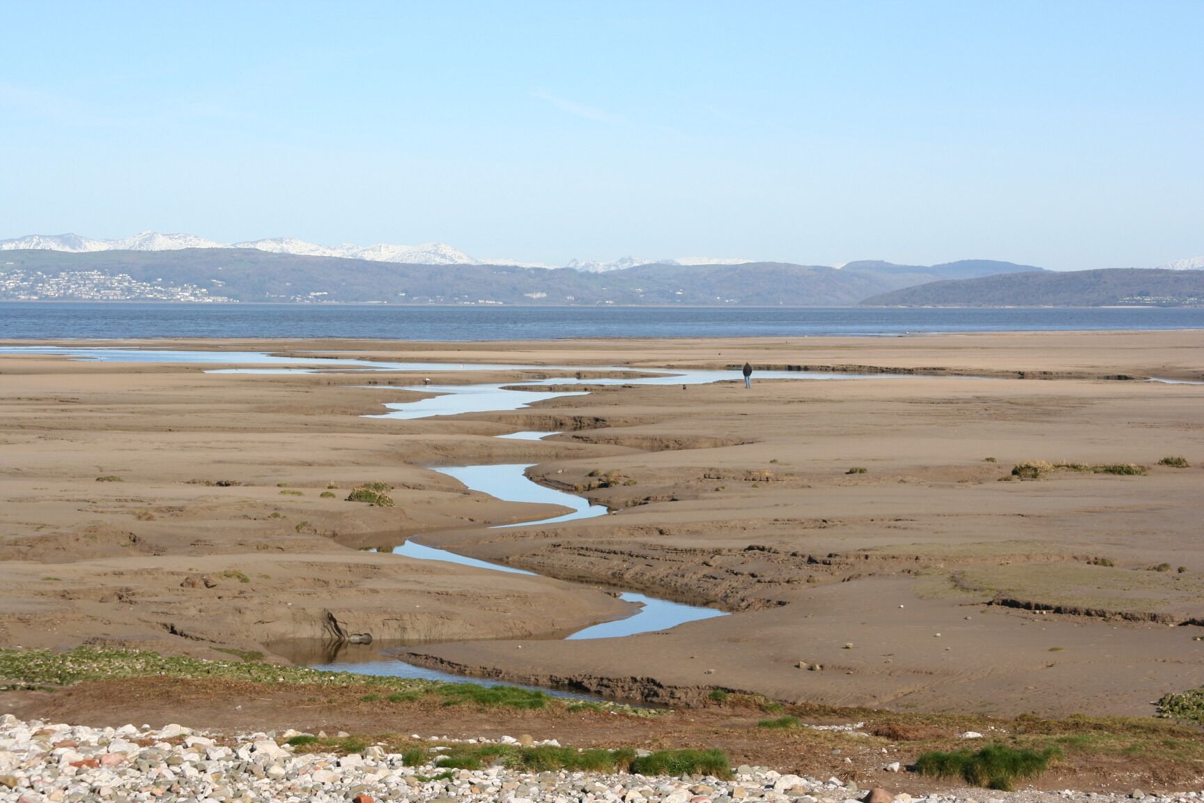 A coastal landscape with a river meandering through a flat terrain, leading to a body of water.