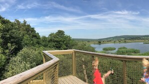 A wooden deck overlooking a lake with a forested landscape. - 1 Lathom Avenue (Morecambe)