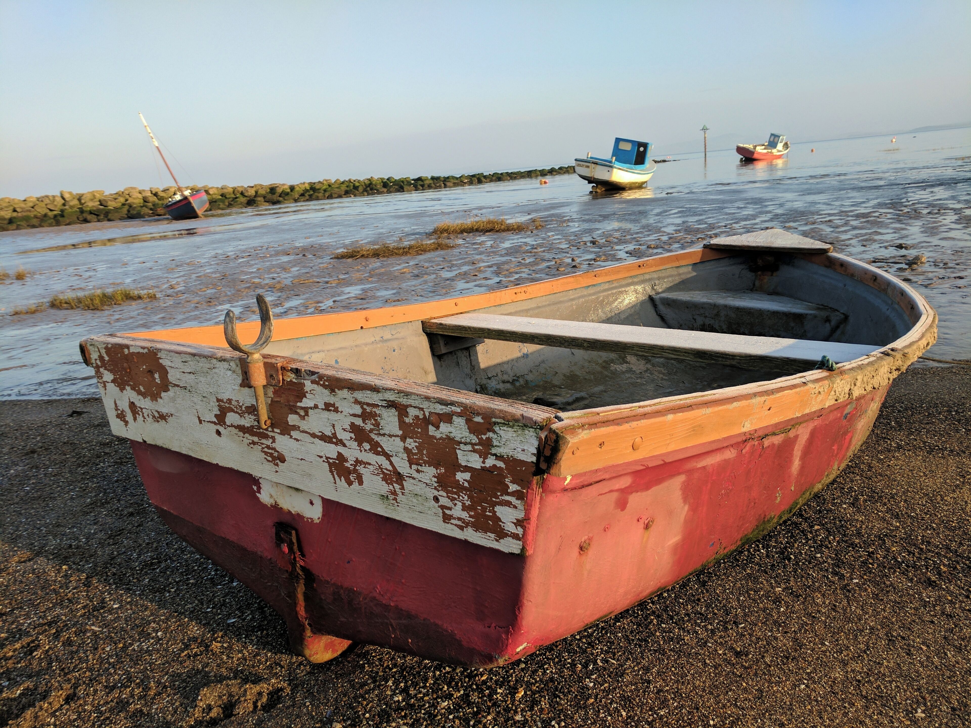 A small, weathered boat with a rusty anchor on a pebbly shore.