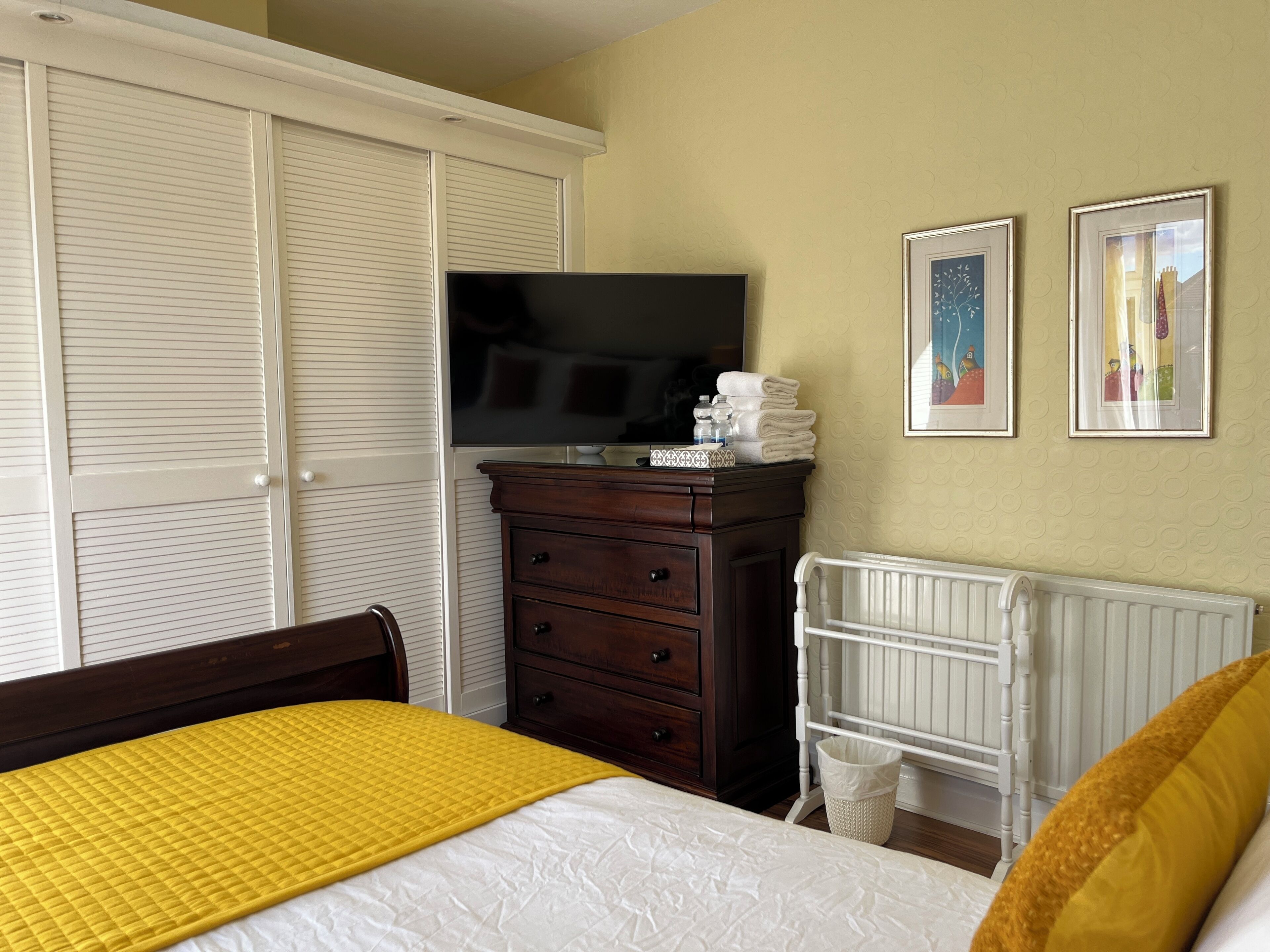 Une chambre à coucher comprenant un lit, une commode, un téléviseur, un berceau et deux tableaux encadrés accrochés au mur.