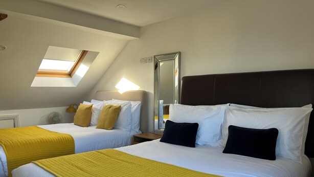 A hotel room with two beds, a skylight, a mirror, and a bedside table. - 1 Lathom Avenue (Morecambe)