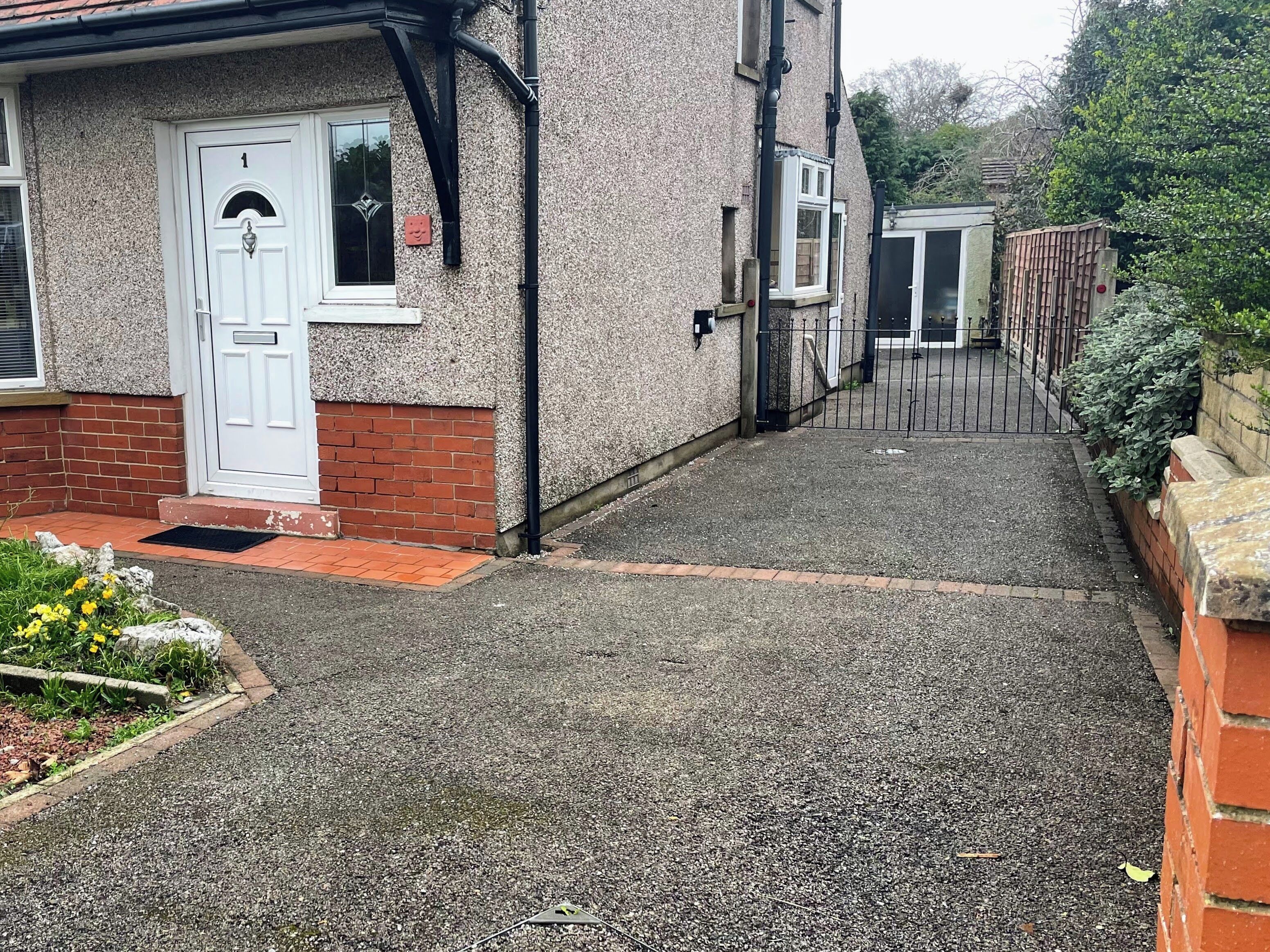 A narrow driveway leading to a house with a white door, a brick wall, and a gravel path.