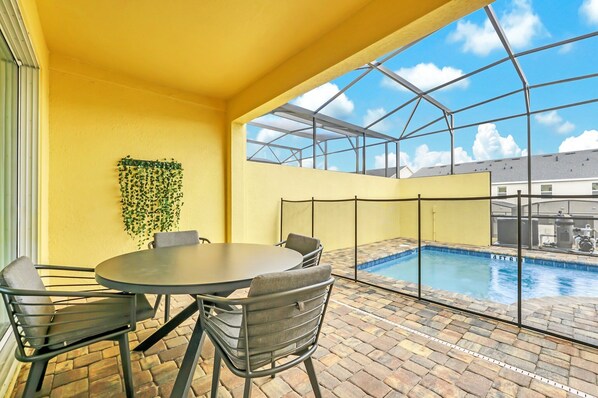 A sunlit patio with a pool, yellow walls, and a glass enclosure.