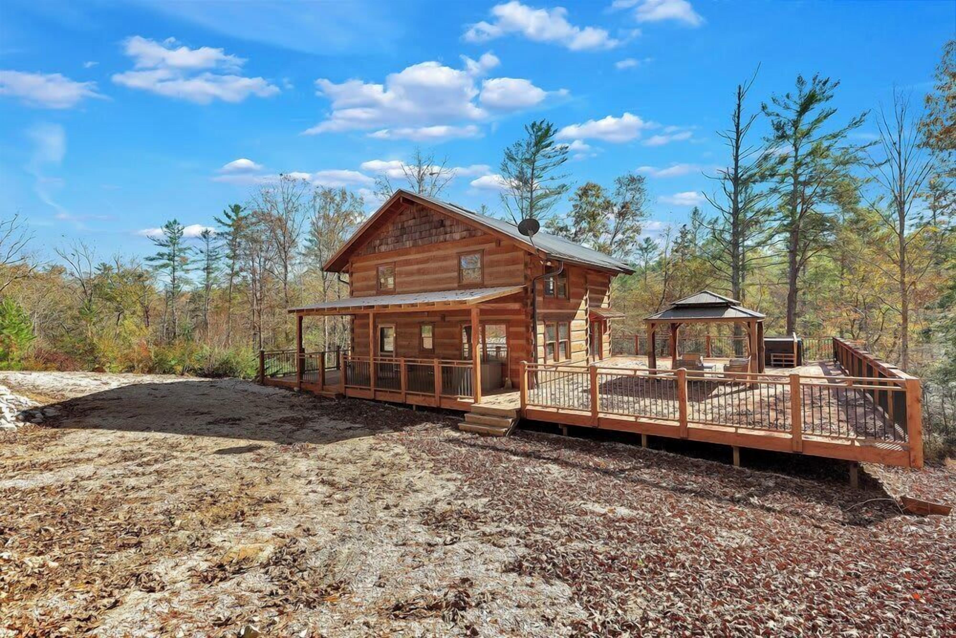 A log cabin with a porch and a deck, surrounded by trees.