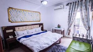 A bedroom with a bed, bedside table, and a small table with a flower vase. - HOTEL GUIKO PALACE (Yaoundé)