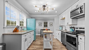 Una cucina moderna con mobili bianchi, un frigorifero color petrolio, elettrodomestici in acciaio inossidabile e una penisola centrale con un lampadario sopra.