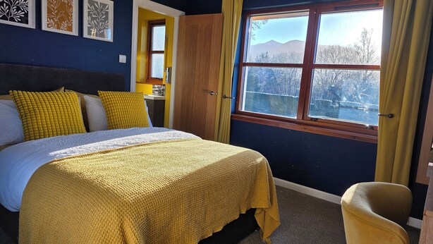 A bedroom with a bed, a chair, a window with a view, and artwork on the wall. - Mizpah Bed & Breakfast (Roybridge)
