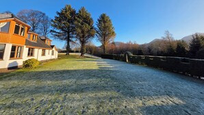 A residential property with a large lawn, a wooden house, and a stone wall. - Mizpah Bed & Breakfast (Roybridge)
