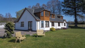 A two-story house with a white exterior and wooden accents, featuring a large front lawn with two wooden benches. - Mizpah Bed & Breakfast (Roybridge)