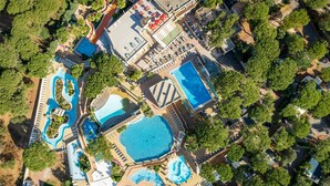 Vista aerea di un resort con diverse piscine, una grande piscina centrale e varie dotazioni, tra cui lettini e ombrelloni.
