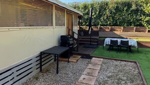 Un'area esterna riparata con tavolo e sedie, un barbecue e un piccolo giardino con prato e vialetto in ghiaia.