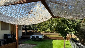 Un patio con una pergola bianca, un barbecue e un tavolo con sedie.