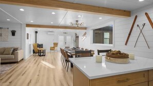 A modern kitchen with wooden beams, a dining area with a large island, and a ski rack on the wall.