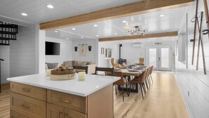 A spacious kitchen with a central island, wooden beams, and a dining area with chairs and a table.