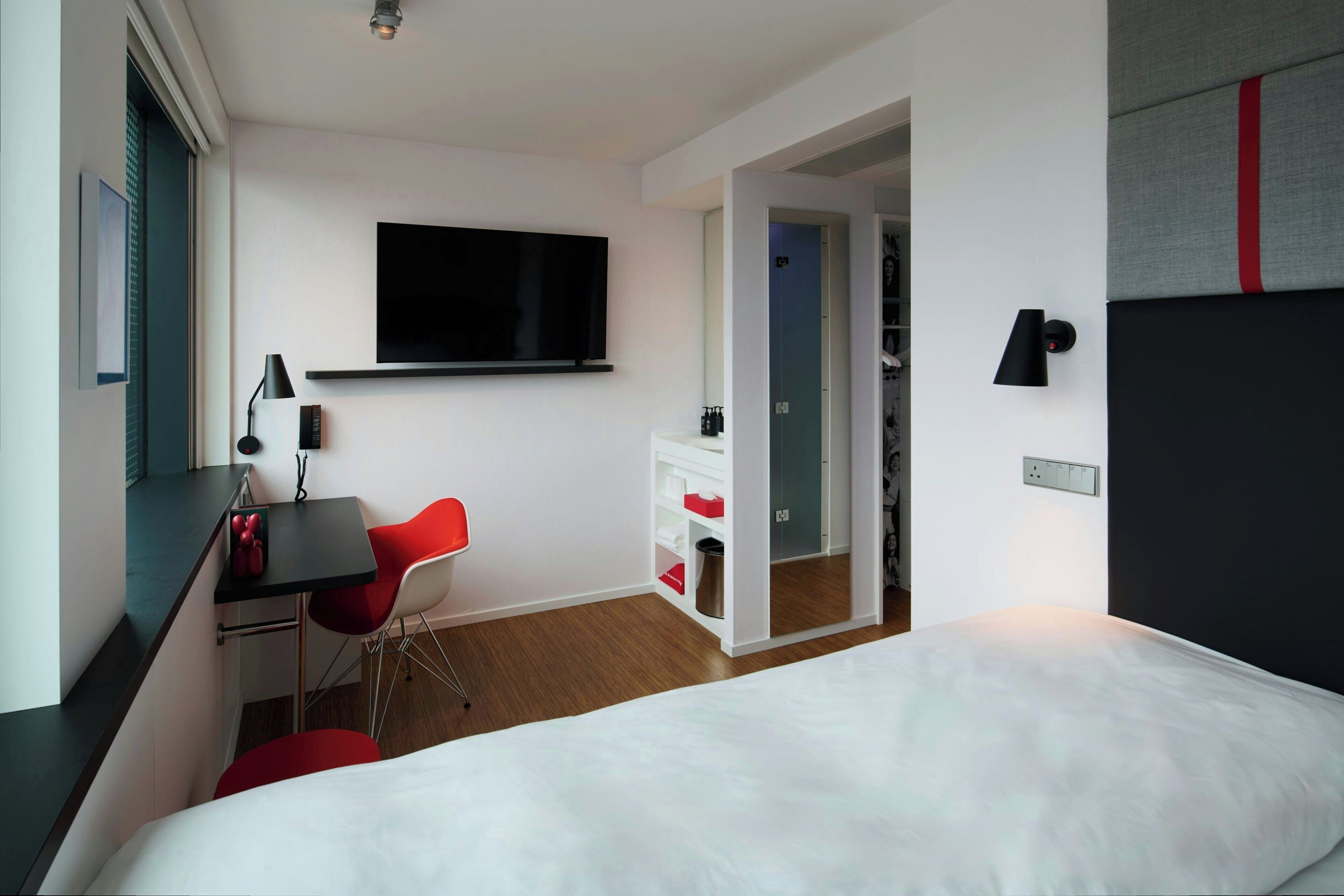 Une chambre d’hôtel moderne équipée d’un lit, d’un bureau avec une chaise, d’une télévision et d’une armoire.