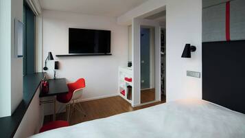 Une chambre d’hôtel moderne équipée d’un lit, d’un bureau avec une chaise, d’une télévision et d’une armoire.