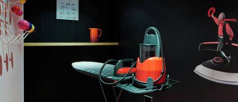 Una habitación con alfombra estampada, una mesa de vidrio con una silla, un taburete rojo, una cafetera de pared, una estantería con una taza y un póster.