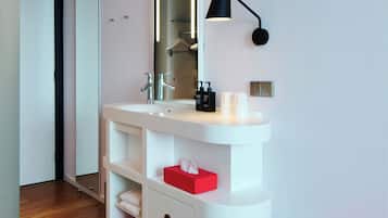 Une salle de bain moderne avec un meuble-lavabo blanc, un grand miroir, une lampe noire fixée au mur et un banc rouge.