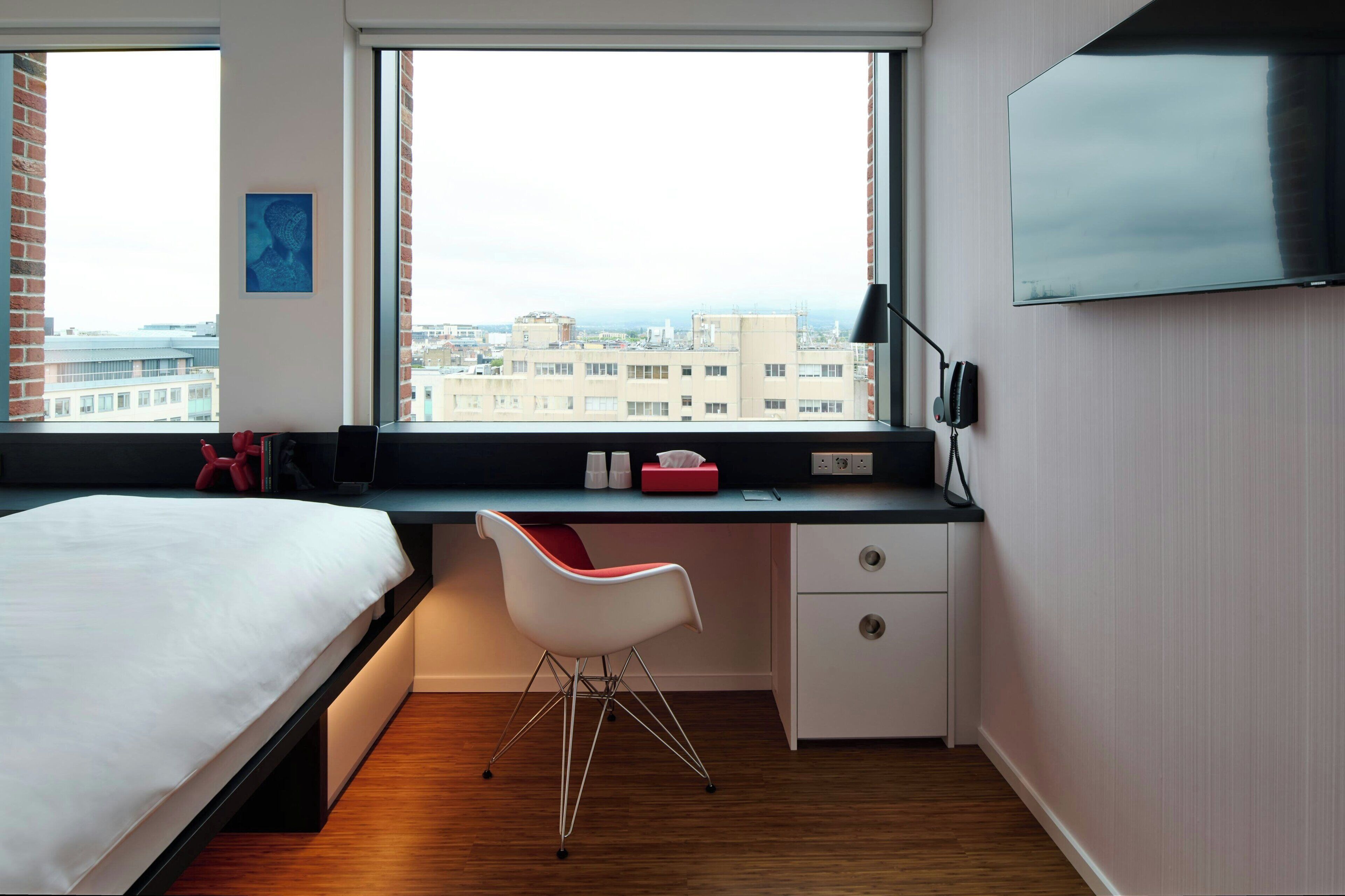 Una habitación de hotel moderna con cama, escritorio, silla, televisor y vista a la ciudad.