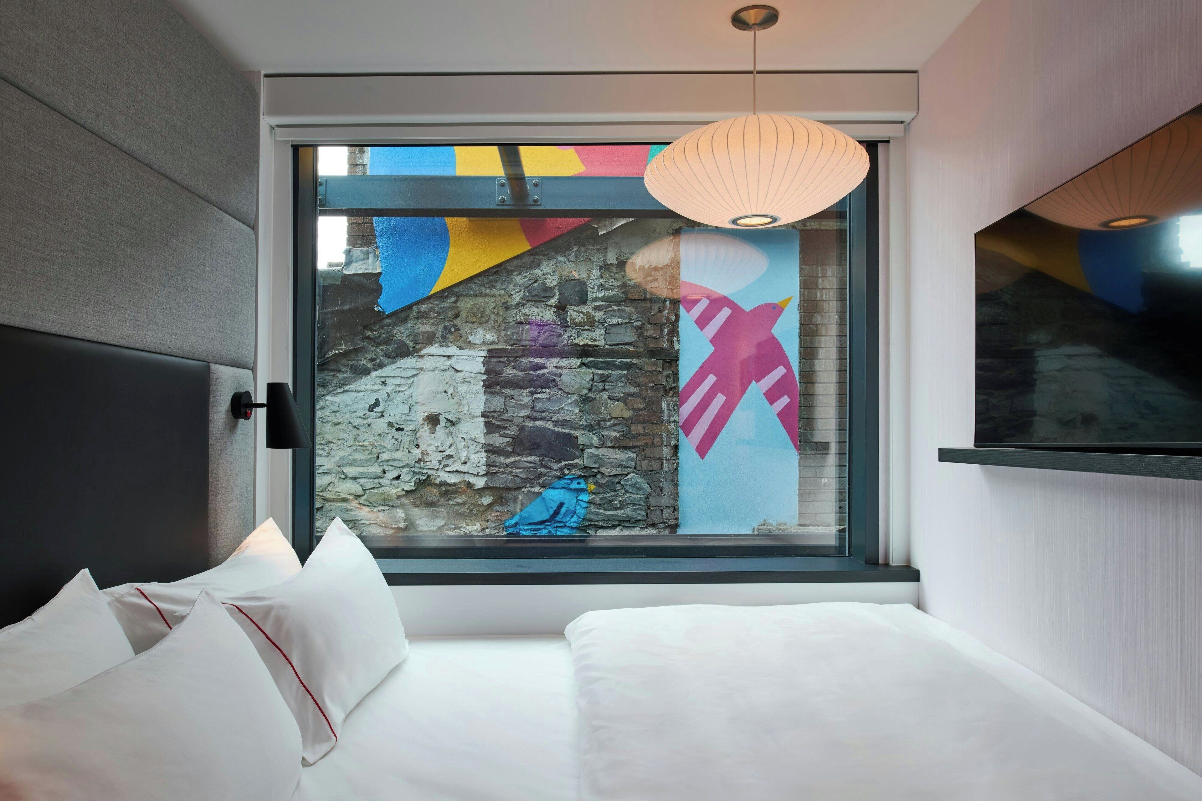 A modern hotel room with a large window, a bed with white bedding, and a decorative bird sculpture on the windowsill.