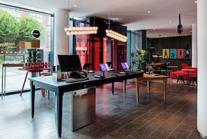 Un moderno vestíbulo de hotel con una recepción, pantallas digitales y una zona de estar con sillas rojas.
